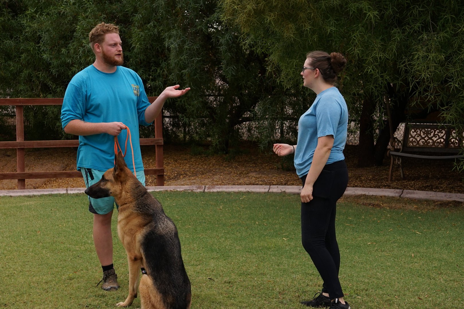 Dog trainer explaining his training methods to a client while a German Shepherd sits attentively beside him on a leash