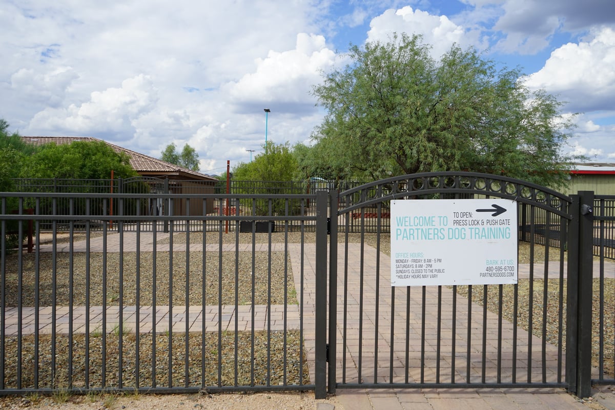 Facility entrance gate with office hours and welcome sign at a Partners Dogs training campus
