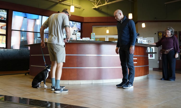 Dog sitting politely on a loose leash beside its owner at the Partners Dogs front desk