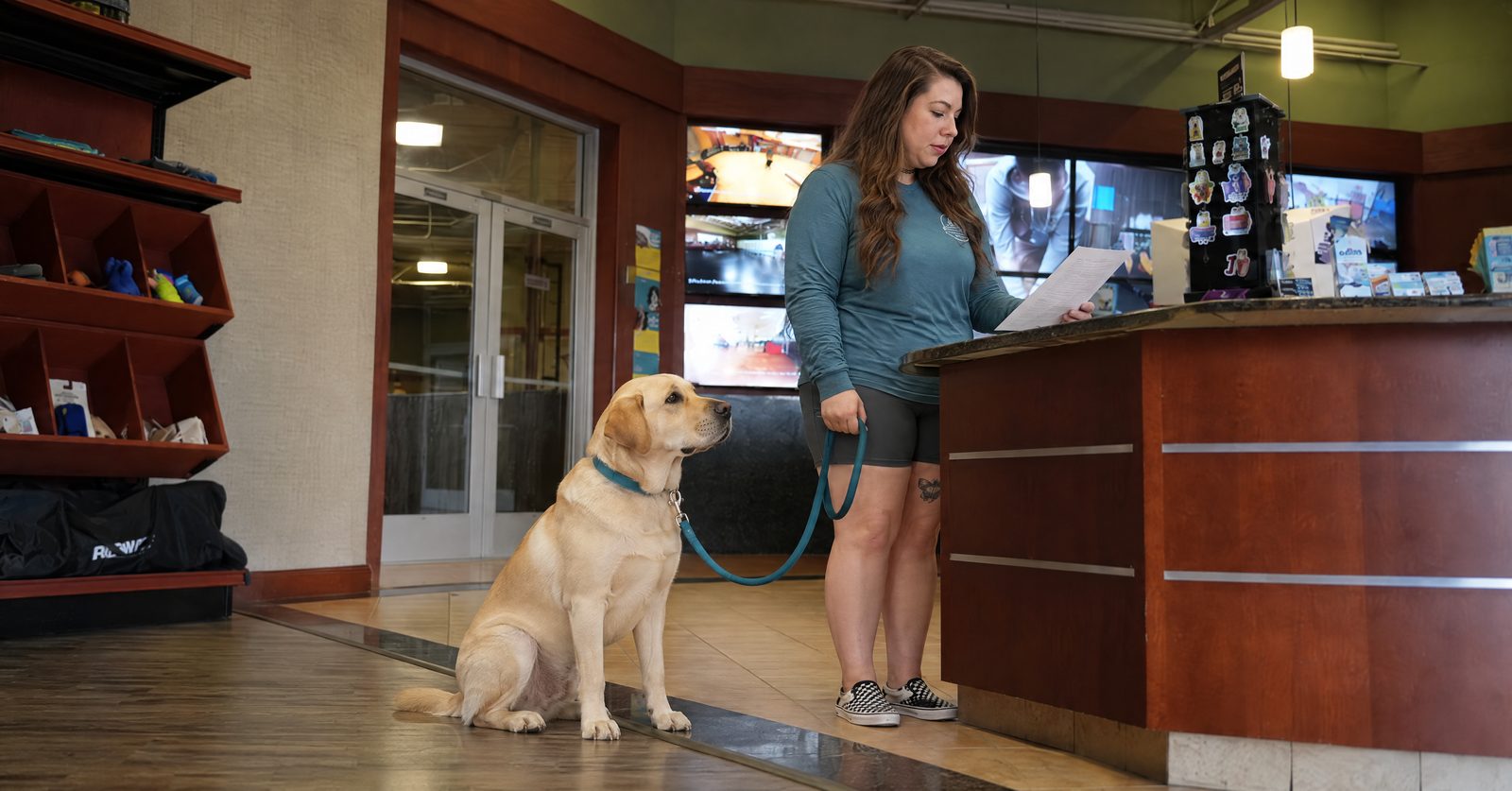 Nicole reviews vaccine records with a Pet Parent beside a calm Labrador at the front desk